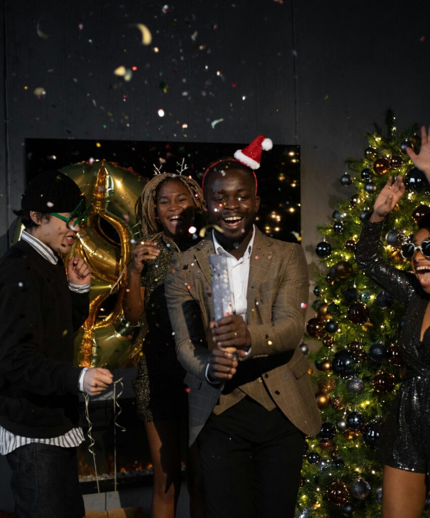 A joyful group of adults celebrating at a festive holiday party with decorations and confetti.